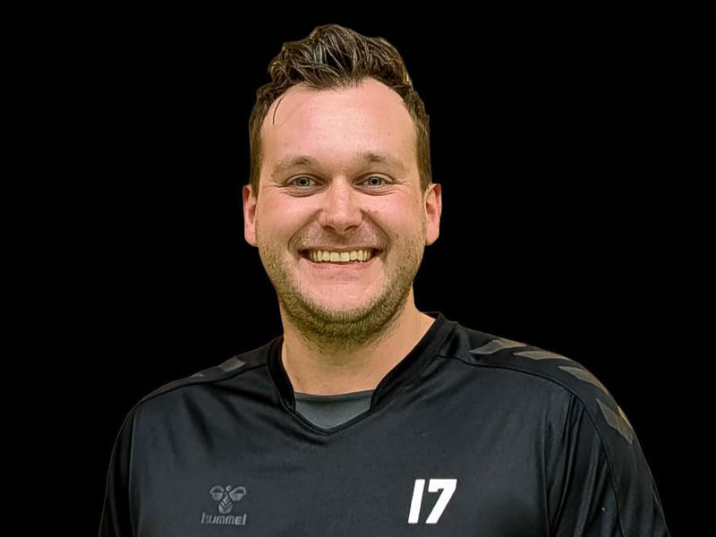 Lachender Handballspieler im schwarzen Trikot vor schwarzem Hintergrund